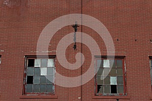 Two large industrial windows with broken frames in a red brick facade