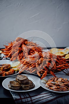 Two large plates with boiled crayfish, a plate with fried tuna steak, boiled shrimps and fried lobster