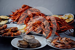 Two large plates with boiled crayfish, a plate with fried tuna steak, boiled shrimps and fried lobster