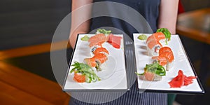 Two large plates with different sushi rolls in the hands of a waiter. Traditional Japanese cuisine concept