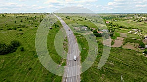 Two large powerful trucks with dump bodies driving along asphalt road in mountainous area near old residential buildings