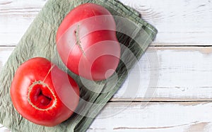 Two large red tomatoes on a light wood background, on a green napkin. Nonstandard ugly food