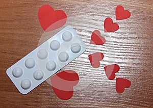 Two large and six small red hearts lie on the surface of a wooden table with a blister of medicine pills, the concept of the need