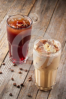 Two large tall glasses with cold coffee sprinkled with almonds and chocolate on wooden table. Coffee beans are scattered