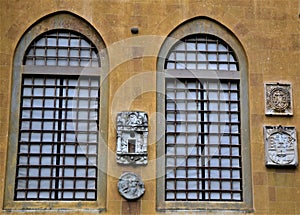 Two large windows with large grates and four stone coats of arms on the wall overlooking the park, of Villa Stibbert in Florence.
