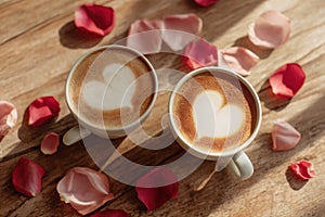 Two latte art heart coffees on rustic wooden table with rose petals