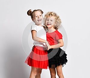 Two laughing blonde kids girls sisters friends in red and white t-shirts and black and red skirts are hugging feel love