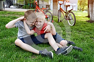 Two laughing boys having fun on the grass. Bicycles in the background