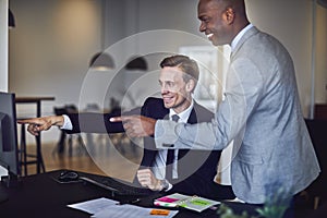 Two laughing businessmen pointing at a monitor in an office