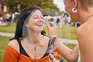 Two Laughing Female Friends Decorating Faces With Glitter At Summer Music Festival 