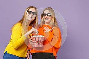 Two laughing young blonde twins sisters girls in 3d imax glasses watching movie film, hold popcorn  on pastel photo