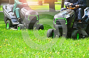 Two lawn mowers trimming green grass on a meadow