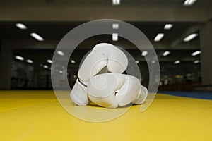 Two leather white Boxing gloves for Kudo wrestling on a yellow tatami on the background of the gym