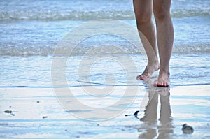 Two legs of lady walking forward on sandy wet beach of the sea with reflection