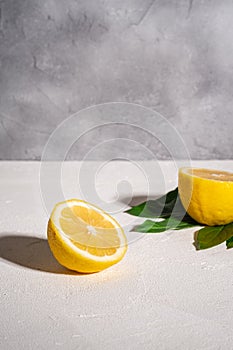 Two lemon slices, tropical citrus fruits with green leaves on white concrete background