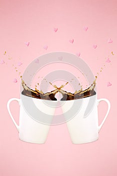 Two levitating coffee mugs with splashes and heart confetti. Coffee concept. Minimal art trend. Solid pink background