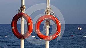 Two lifebuoys hang on a pole in the sea, people are bathing