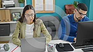 Two lifestyle professionals, man and woman coworkers, working together using computer and laptop in an elegant office interior