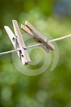 Two light wooden clothes pegs hanging on clothesline in sunlight, green blurry background