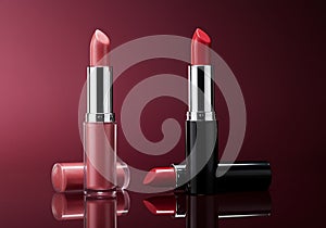 Two lipsticks displayed with caps and applicators on reflective surface