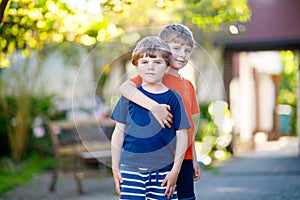 Two little active school kids boys, twins and siblings hugging on summer day