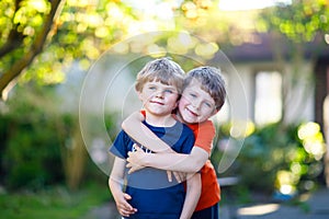 Two little active school kids boys, twins and siblings hugging on summer day