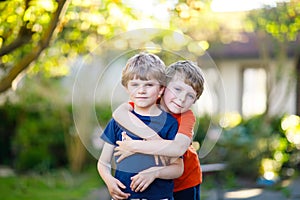 Two little active school kids boys, twins and siblings hugging on summer day