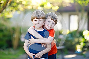 Two little active school kids boys, twins and siblings hugging on summer day