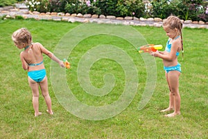 Two little adorable girls playing with water guns