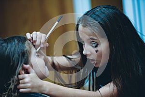 Two little american sisters girls kids prepare to Halloween holiday making dark scary makeup on face with emotions