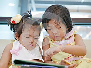 Two little Asian baby girl, sisters, sitting and watching a smartphone together, while waiting for her mother