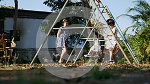 Two little Asian baby girls, 3 and 2 years old sisters, riding swings at a playground with help from their mother