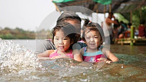 Two little Asian baby girls, sisters, enjoys playing water in a river with her auntie