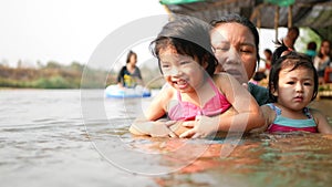 Two little Asian baby girls, sisters, enjoys playing water in a river with her auntie - playing outdoor and engaging with nature