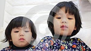 Two little Asian baby girls, sisters, paying all their attention watching a smartphone at home