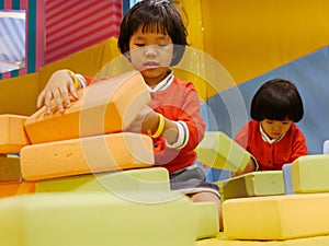 Two little Asian baby girls, sisters, stacking up foam building bricks / blocks together at an indoor playground