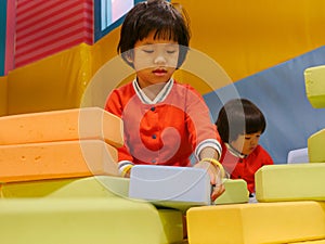 Two little Asian baby girls, sisters, stacking up foam building bricks / blocks together at an indoor playground