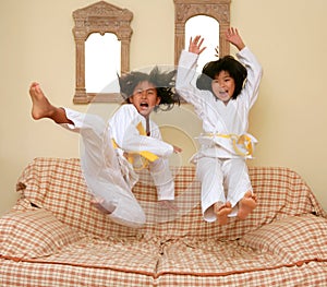 Two little asian judo gils jump on sofa