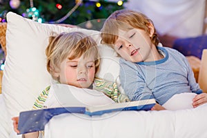 Two little blond sibling boys reading a book on Christmas