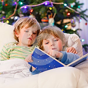 Two little blond sibling boys reading a book on Christmas