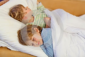 Two little blond sibling boys sleeping in bed