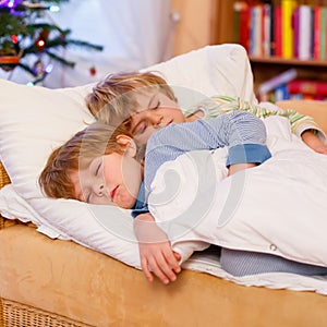 Two little blond sibling boys sleeping in bed on Christmas