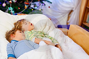 Two little blond sibling boys sleeping in bed on Christmas