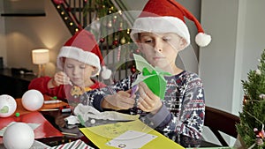 Two little boy preparing for Christmas cutting out paper decorations and garlands. Winter holidays, family time together