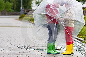 Two little boys, best friends and siblings walking with big umbrella outdoors on rainy day. Preschool children having