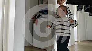 Two little boys are captured in slow motion footage, running with smiles on their faces on a wooden floor in a long corridor.