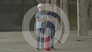Two little boys with dirty faces standing in the abandoned building with the fire extinguisher looking at camera