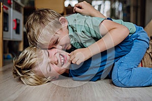 Two little boys fighting on the floor, brothers having fun at home. Concept of sibling relationship and brotherly love.