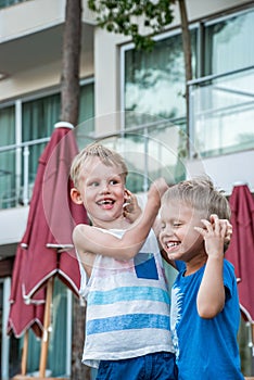 Two little boys are laughing and playfully holding each others ears in seaside resort