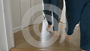 Two little boys with mother are seen running and playing in slow motion on a wooden floor in a long corridor.